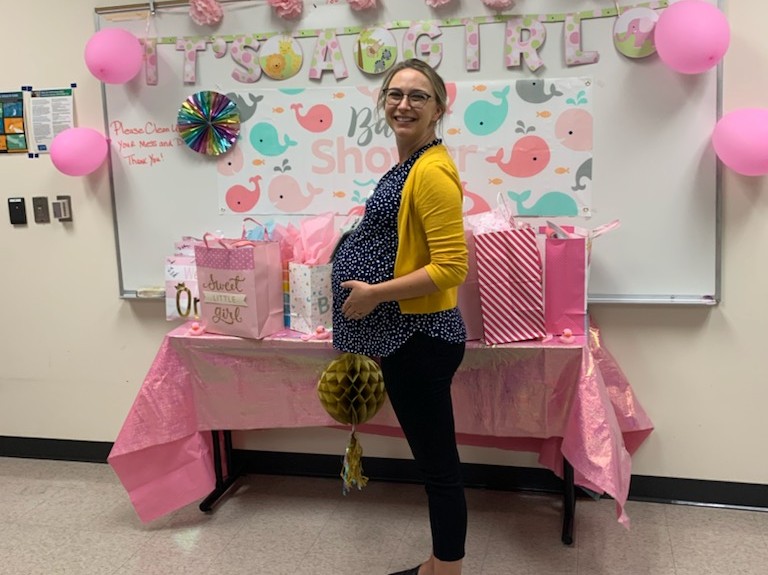person standing in front of baby shower sign holding pregnant belly