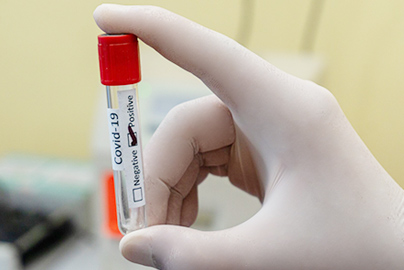 A gloved hand holding a vial with a COVID-19 test strip in it.