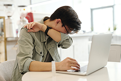 Young man at a computer, coughing into his elbow.