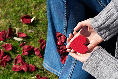 A woman sitting cross-legged holding a paper heart with rose petals dropped on the ground near her.