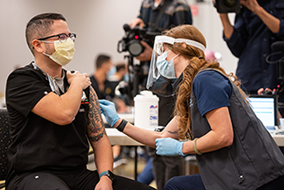 A man is receiving a vaccination with media cameras pointed at him.