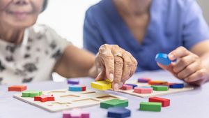 This image shows a senior individual engaging in a cognitive therapy activity using a wooden shape-matching puzzle, a common practice in memory care settings to support those with dementia.