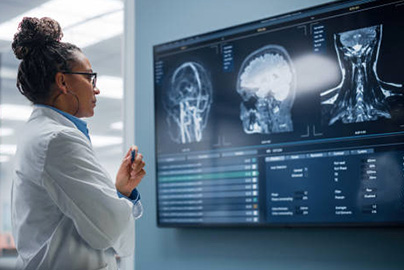 woman in white coat looking at imaging results on a screen