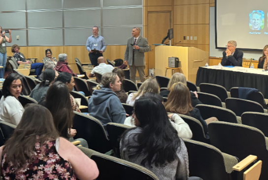 Lecture hall with presenters and panelists at the front, participating guests in the audience
