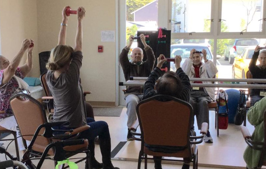 group of older men and women in wheelchairs holding small dumbbells over their heads