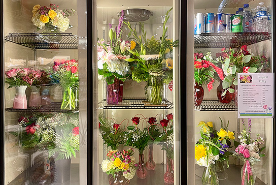 A display of flowers and bouquets in refrigerator, along with some cold drinks.