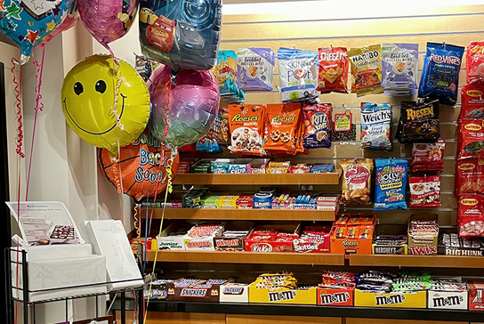 Gift shop shelf with balloons, candy and snacks.