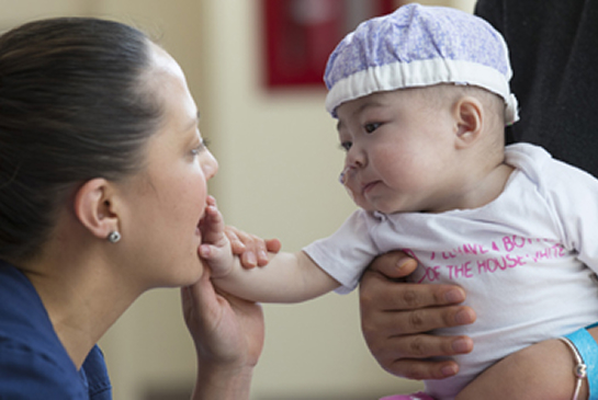 A nurse in scrubs interacts warmly with an infant patient in a hospital setting.