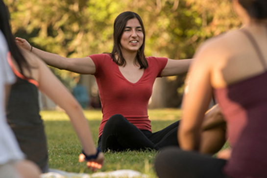 A woman smiles while doing yoga outdoors in a park with a group.