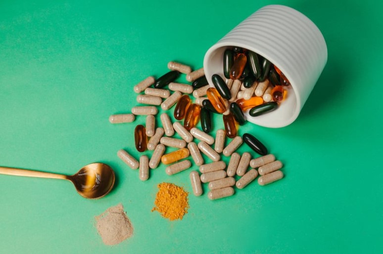 Vitamins and supplements scattered on green background.