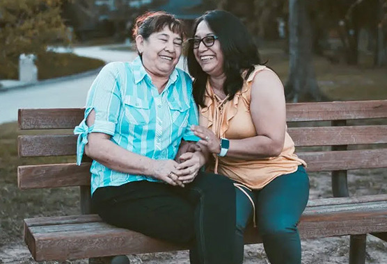 Two women holding each other and smiling on a park bench.