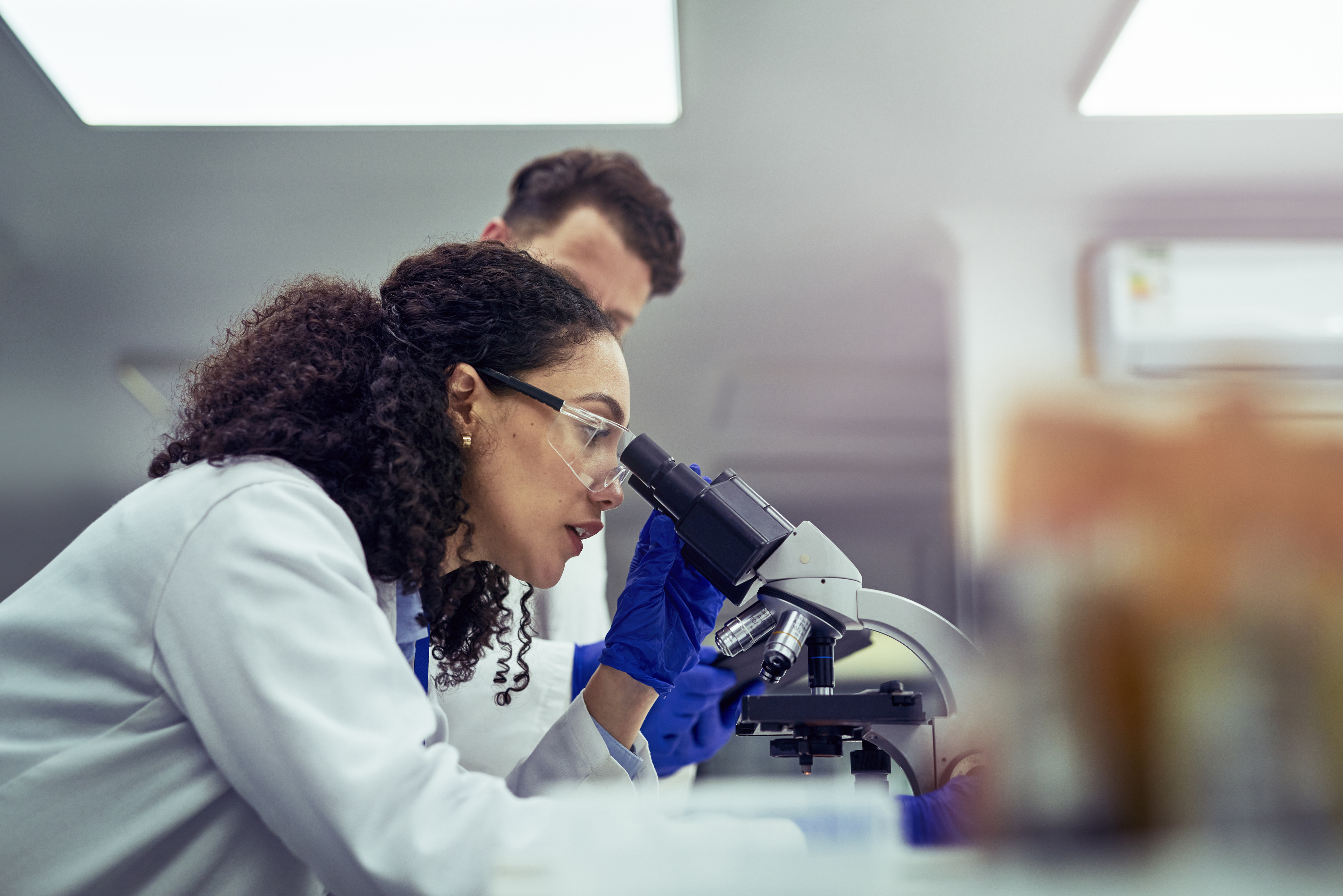 Two scientists in lab coats looking at microscope.