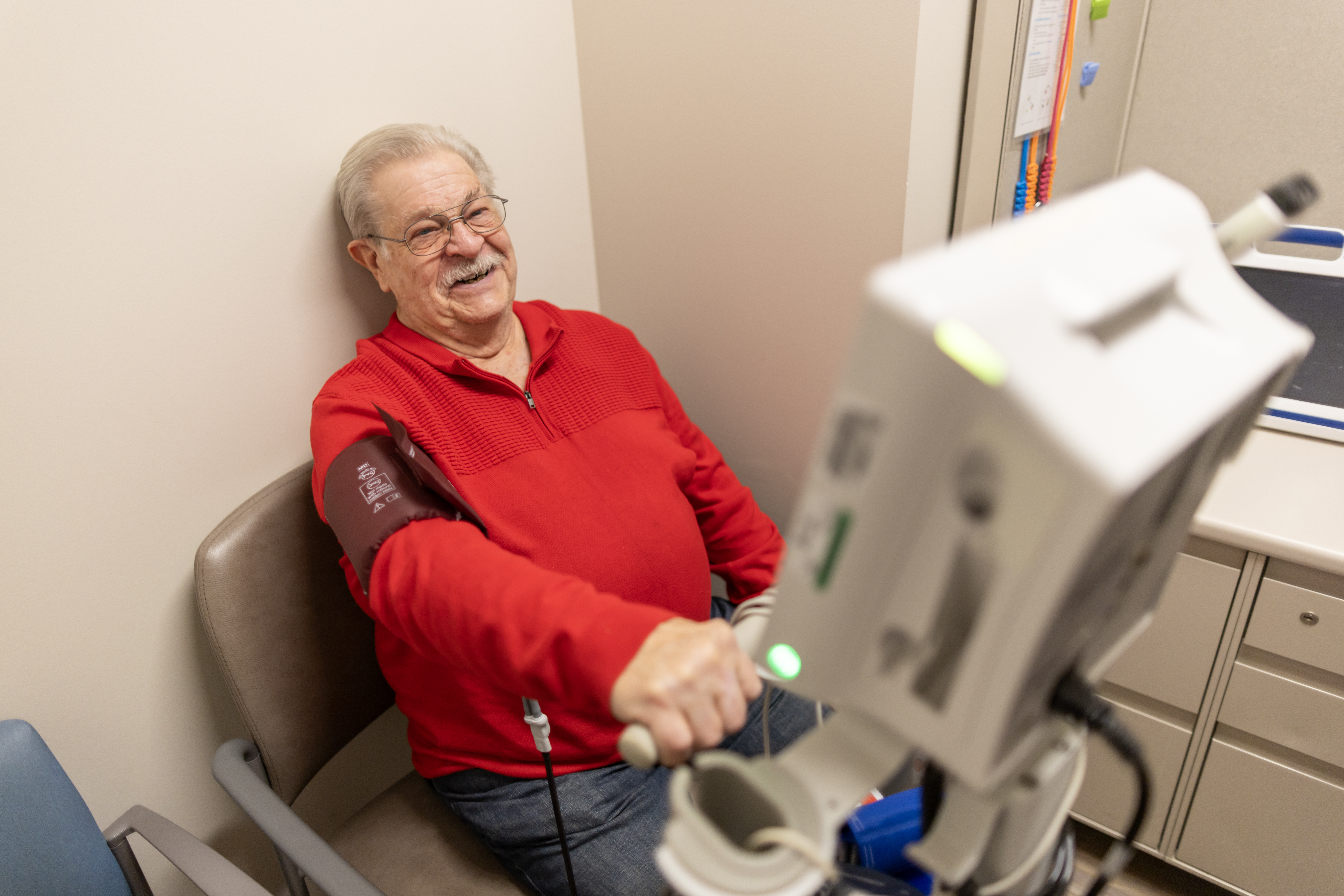 Elderly male patient smiling holding blood pressure monitor.