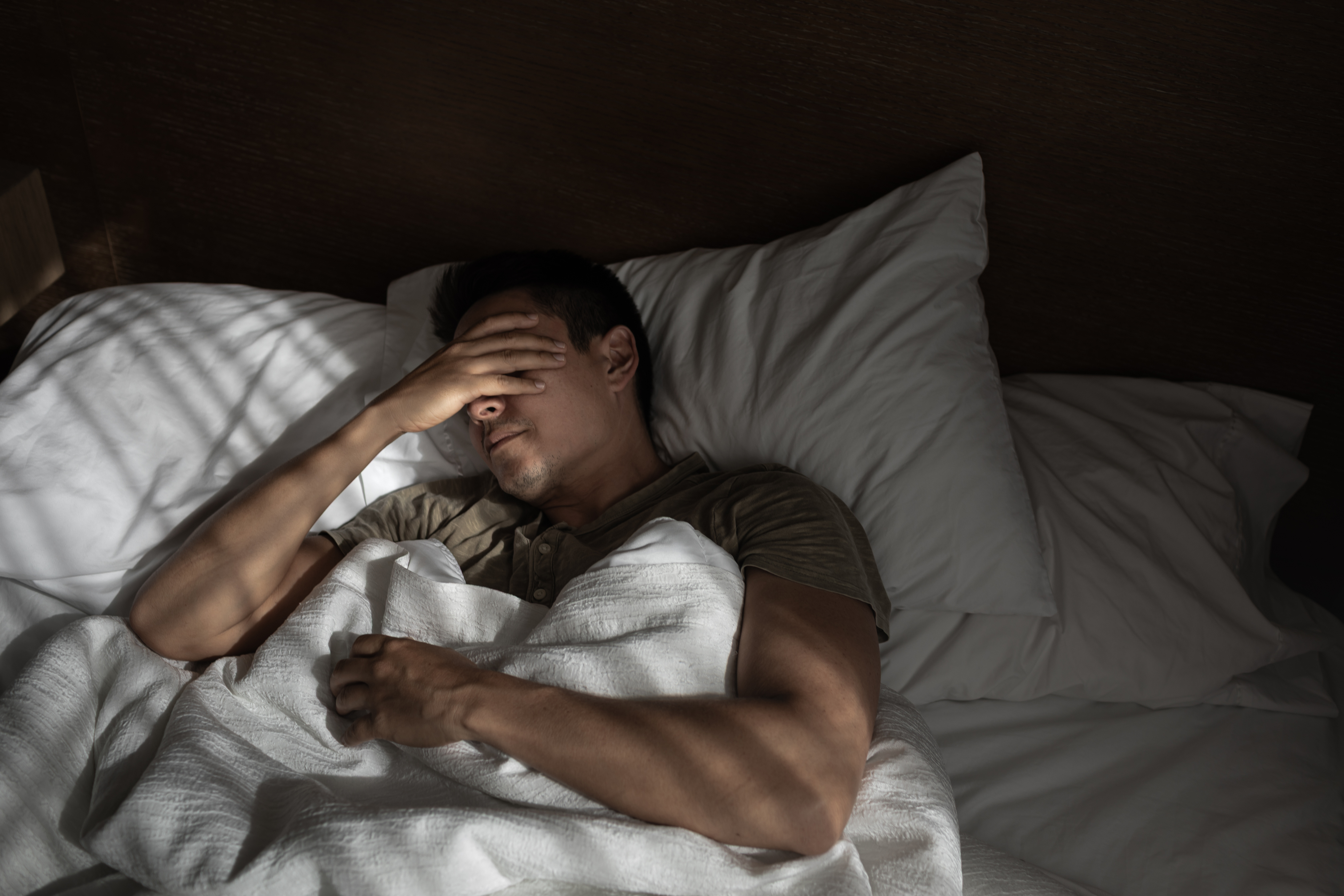 Man with hand over face while in bed.