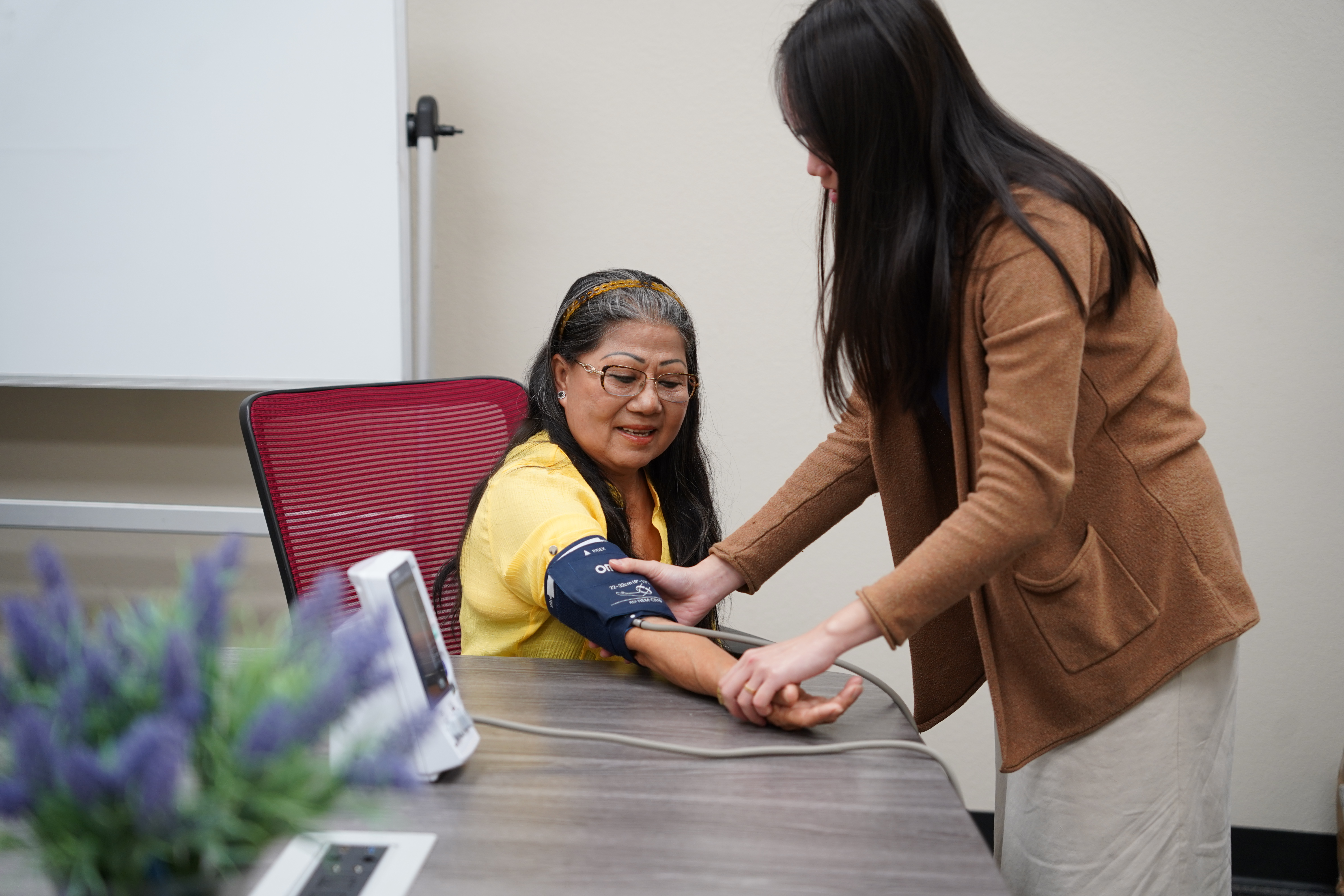 Older asian woman with blood pressure monitor on next to younger woman.