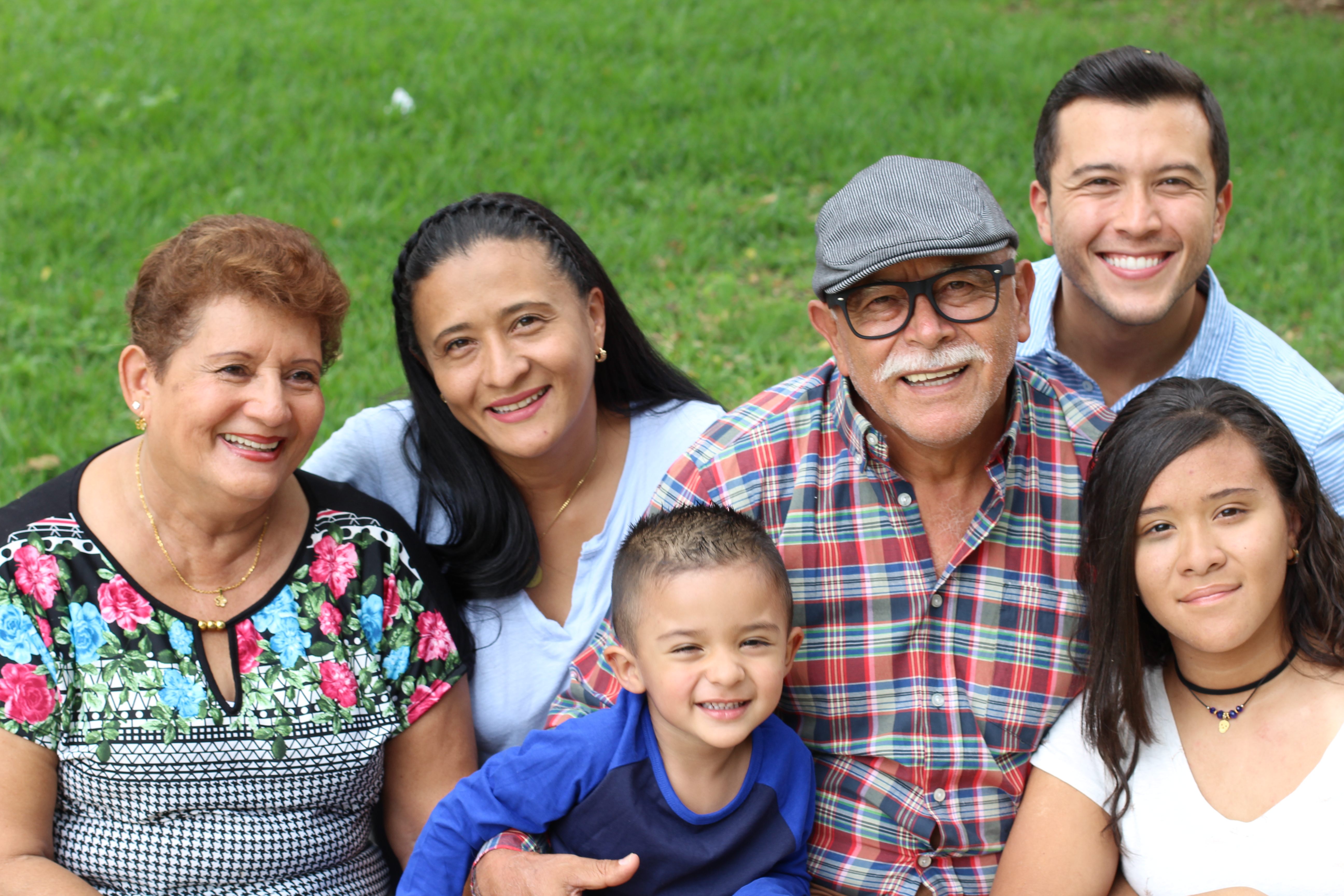 Latino family sitting on grass smiling.