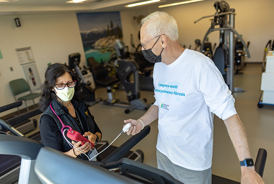 A man on a treadmill being supervised by a healthcare worker. 