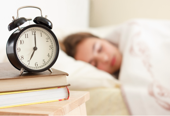 Stock image of person sleeping with alarm clock next to them.