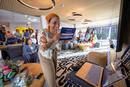 smiling woman holding a sign towards laptop