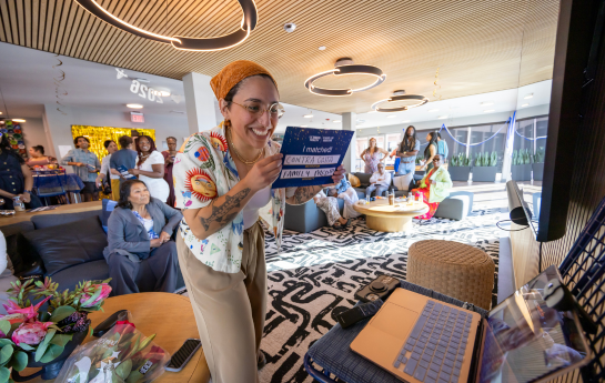 smiling women holding a sign towards laptop