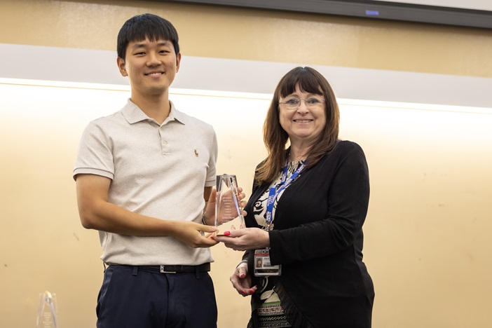 a woman presents a clear plaque to a young man in a polo shirt