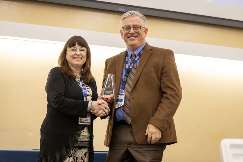 woman hands a clear plaque to a man in a dark gray suit
