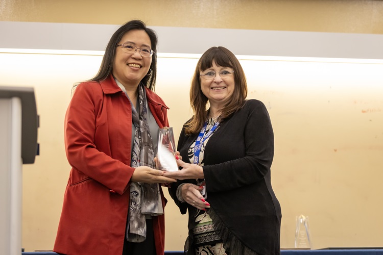 a woman hands a clear plaque to a woman in a red jacket