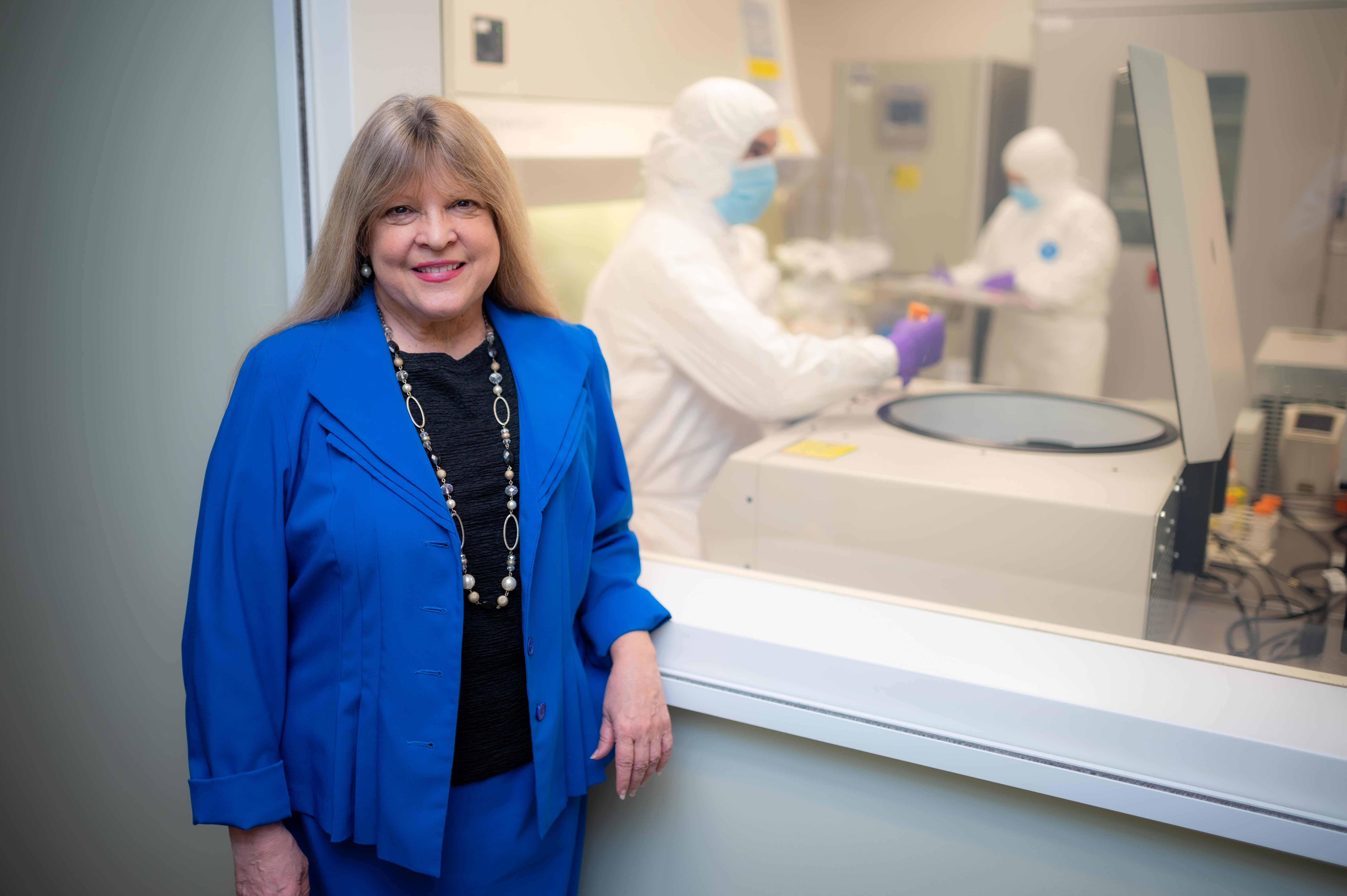 Blond woman in a white coat stands in front of a lab