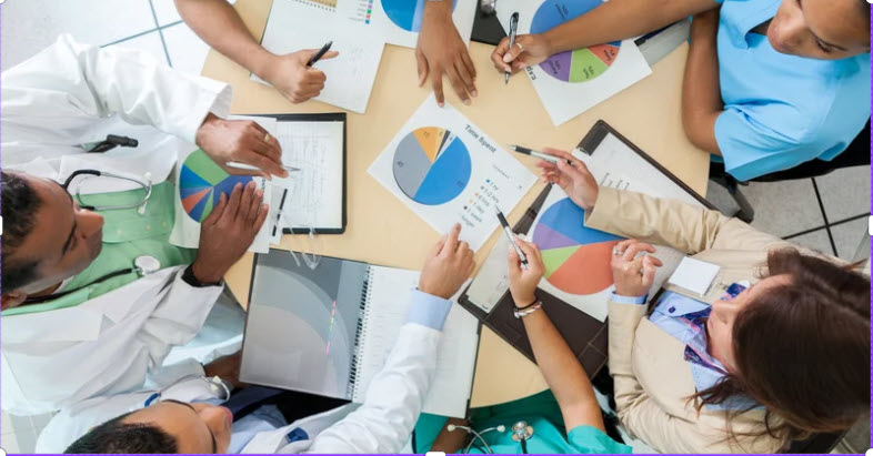 overhead shot of a group of people around a table, comparing charts.