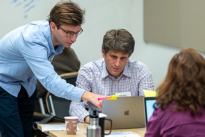 An instructor pointing at the screen of a student's laptop.