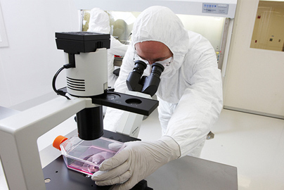 A man wearing a biological safety suit looking into a microscope.