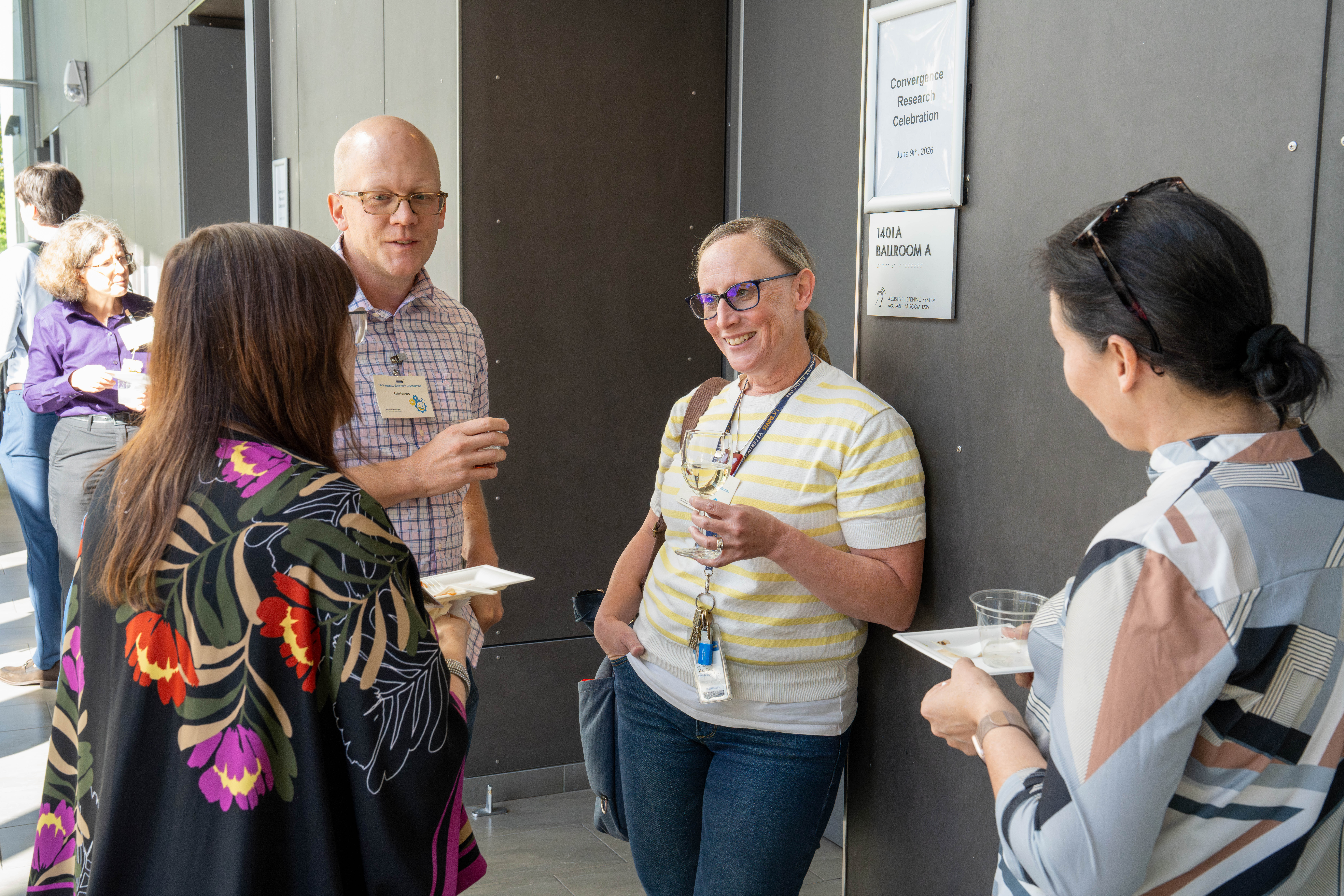 Four people stand together enjoying food and beverages