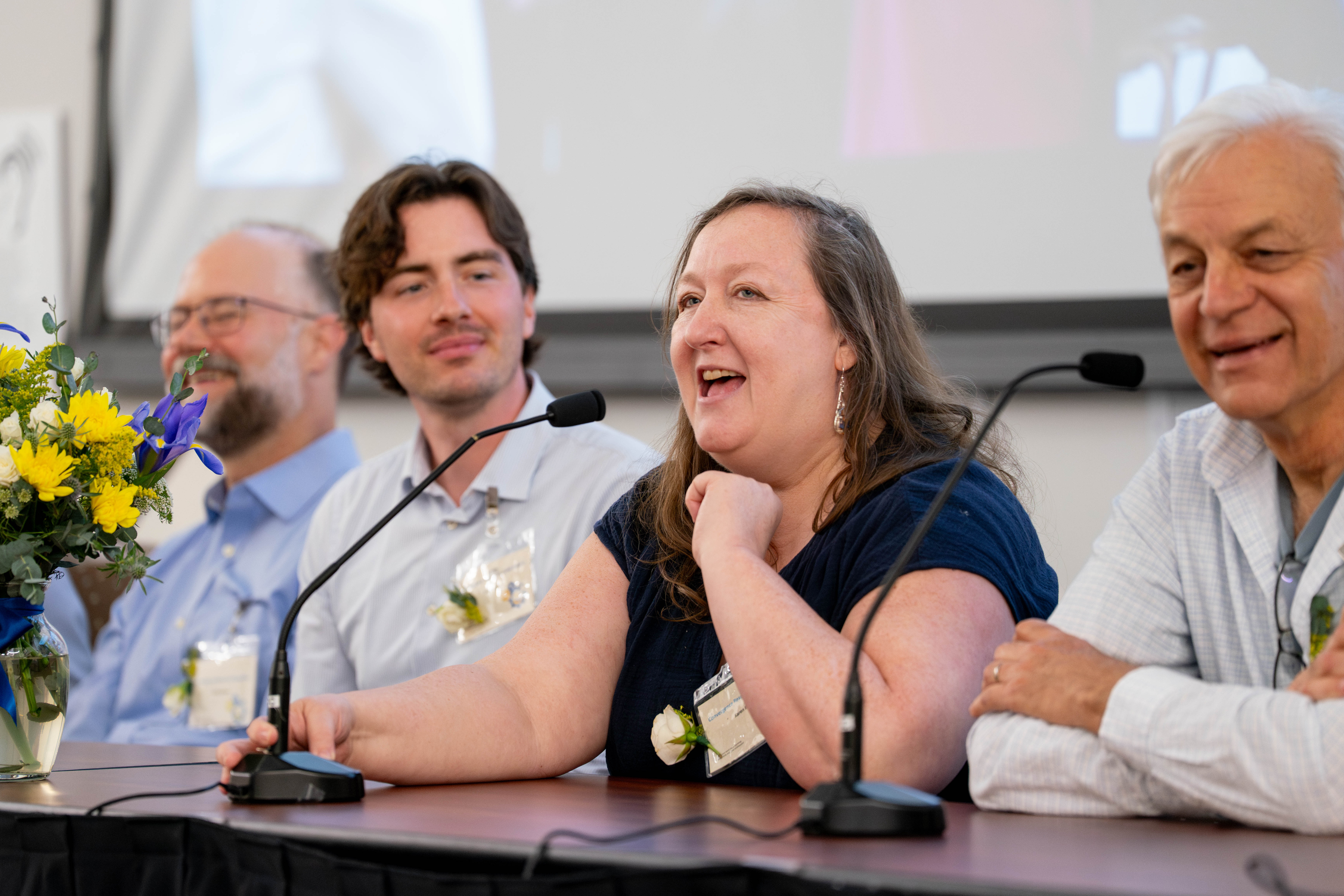 Four professionals sit at a table with microphones, the woman who is third from the left addressing is speaking with a large smile.