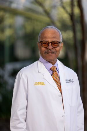 Portrait of James Boggan wearing a white UC Davis Health lab coat and patterned tie, standing outdoors with campus greenery softly blurred in the back