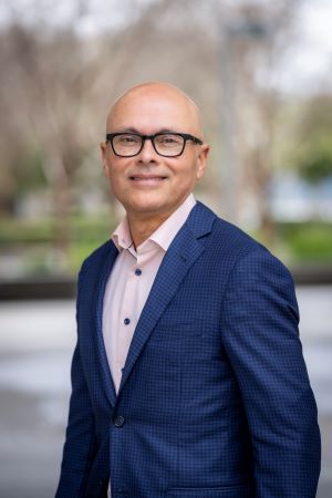 Portrait of Luis Fernando Santana wearing glasses and a dark jacket, photographed outdoors with greenery softly blurred in the background.