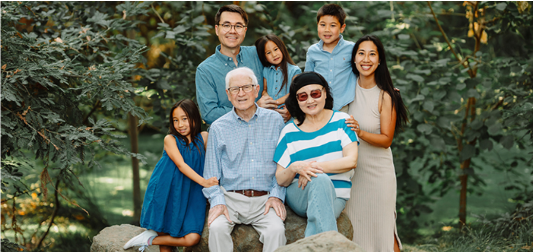photo of Charlotte Zhang with her family, all smiling at the camera in an outdoor setting with visible rocks and trees.