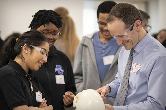 Dr. Arnaud Bewley shows students from Sacramento High School how to repair fractured facial bones on polymer skulls.