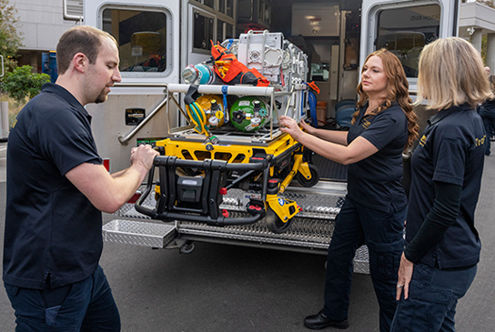Nurses and EMT workers with a gurney at an emergency vehicle.
