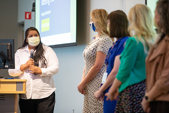 A woman delivering a presentation to a large group of nurses in a meeting room.