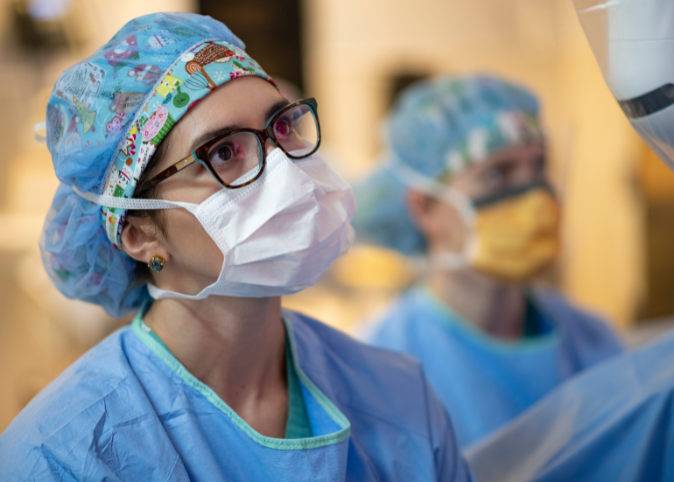 A female surgeon looks up and to the right in a surgery room.