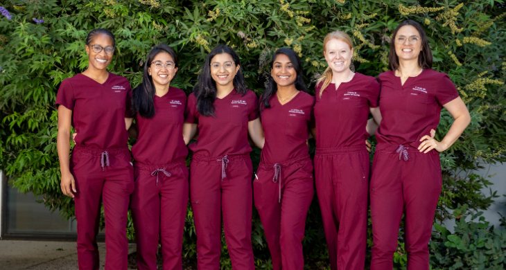 2025 class of OBGYN residents smiling near trees and bushes.