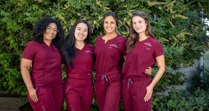 2026 class of OBGYN residents smiling near trees and bushes.