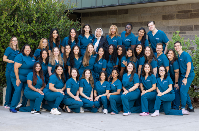 Group photo of OBGYN residents outdoors by brick builidng; they are smiling and wearing scrubs.