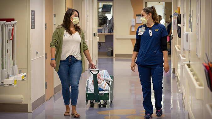 Mom with child walking down hospital hall with care team member.
