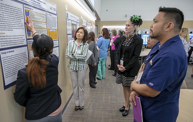 Residents show off their scholarly project posters in conference presentation setting.