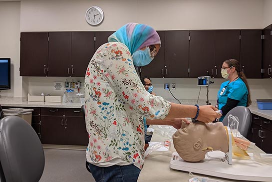 Resident practices simulation on manikin head in education simulation classroom.