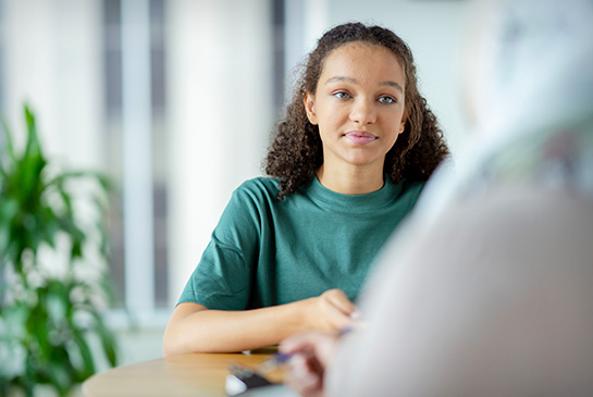 Young teen at a table facing a provider, stock