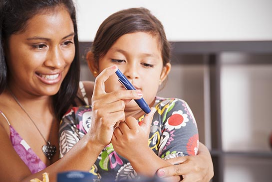 Mother helps diabetic daughter test blood from finger.