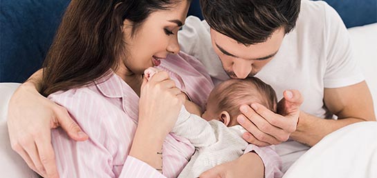 New mother and father kiss baby's head while breastfeeding.