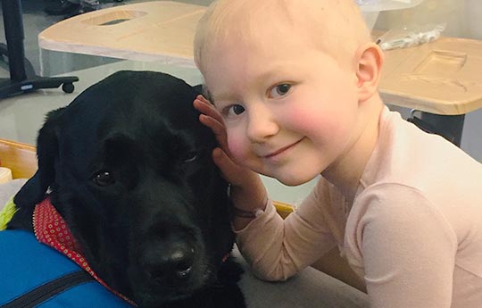 Pediatric cancer patient, Peyton, with black Lab therapy dog. 